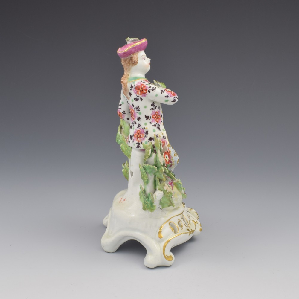 An 18th-century Bow soft-paste porcelain figure depicting an allegorical youth standing beside floral bocage on a pierced gilded scroll base. View III