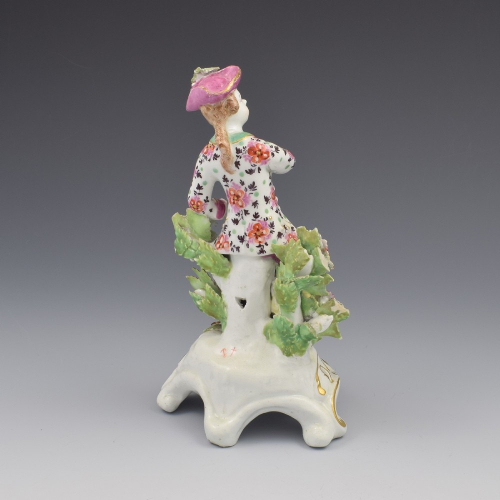 An 18th-century Bow soft-paste porcelain figure depicting an allegorical youth standing beside floral bocage on a pierced gilded scroll base. View IV