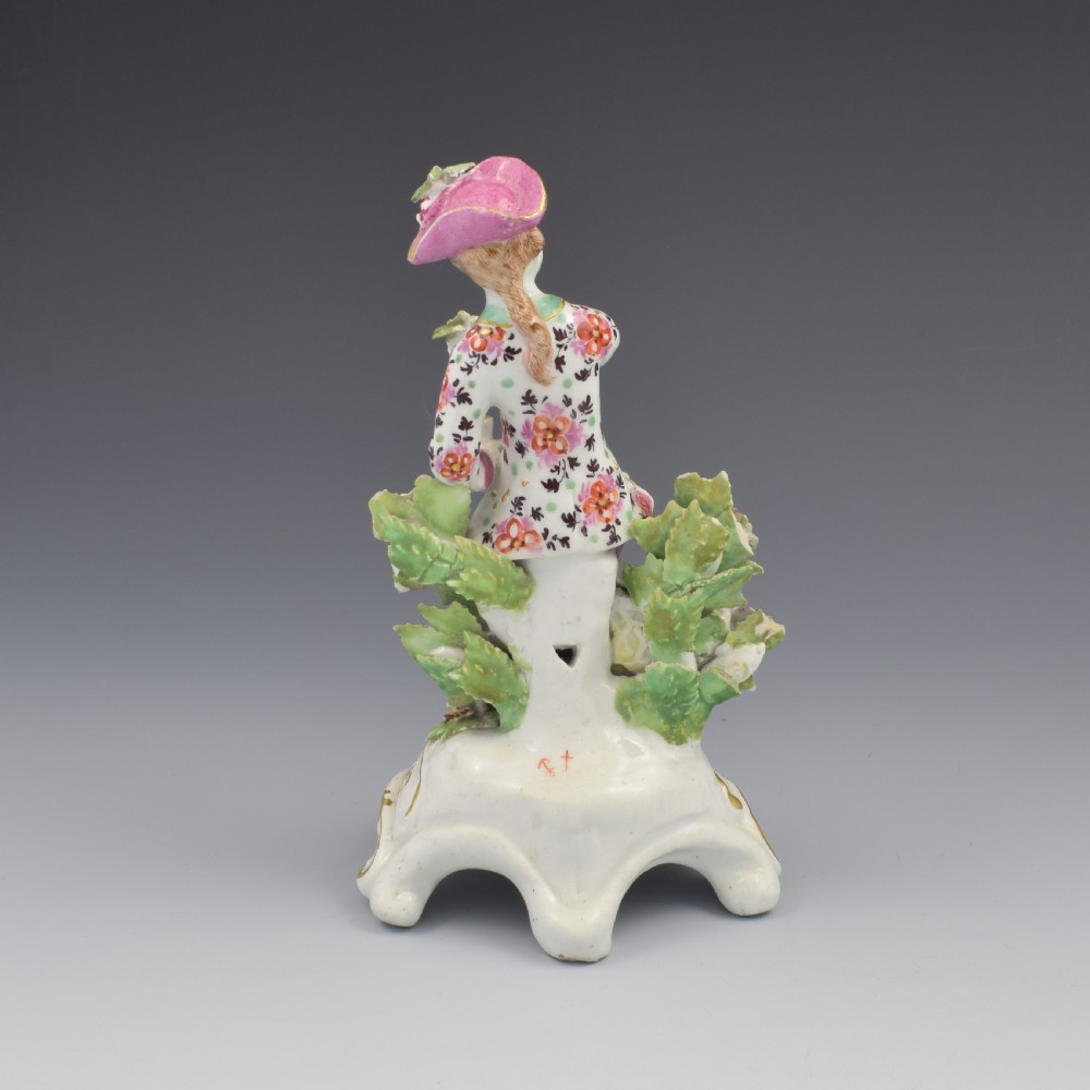 An 18th-century Bow soft-paste porcelain figure depicting an allegorical youth standing beside floral bocage on a pierced gilded scroll base. View V