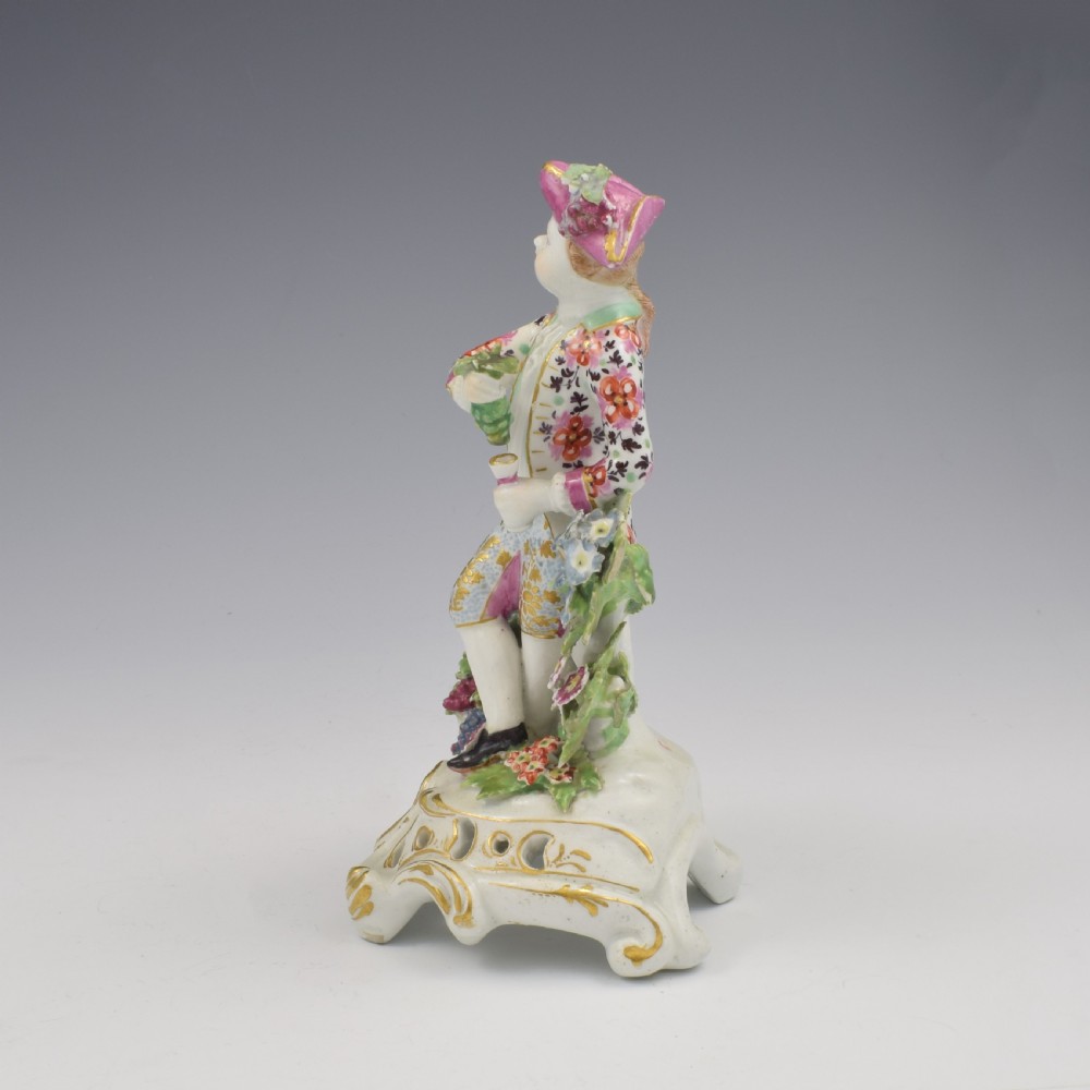 An 18th-century Bow soft-paste porcelain figure depicting an allegorical youth standing beside floral bocage on a pierced gilded scroll base. View VI