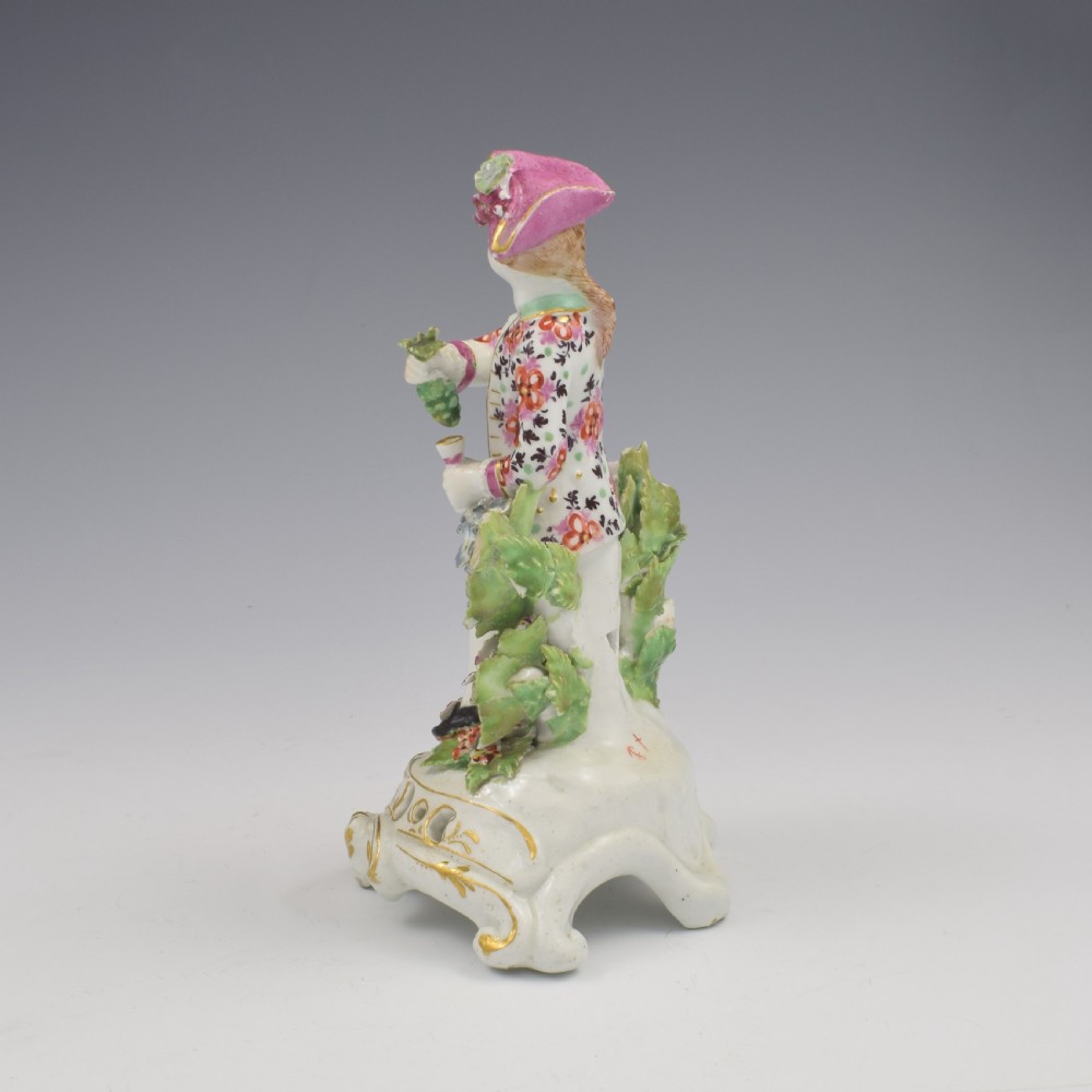 An 18th-century Bow soft-paste porcelain figure depicting an allegorical youth standing beside floral bocage on a pierced gilded scroll base. View VII