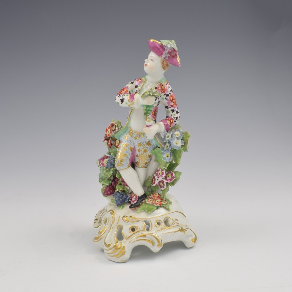 An 18th-century Bow soft-paste porcelain figure depicting an allegorical youth standing beside floral bocage on a pierced gilded scroll base. View VIII