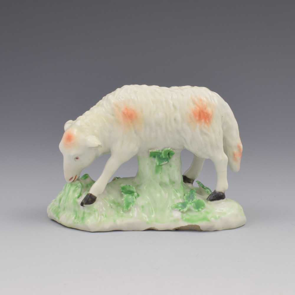 An 18th-century Derby porcelain figure depicting a white grazing ewe with orange flecks on a green leaf-patterned base.