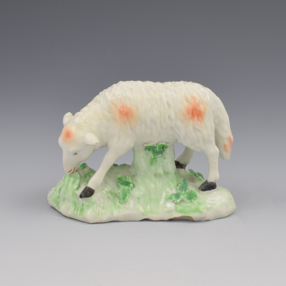 An 18th-century Derby porcelain figure depicting a white grazing ewe with orange flecks on a green leaf-patterned base. View II