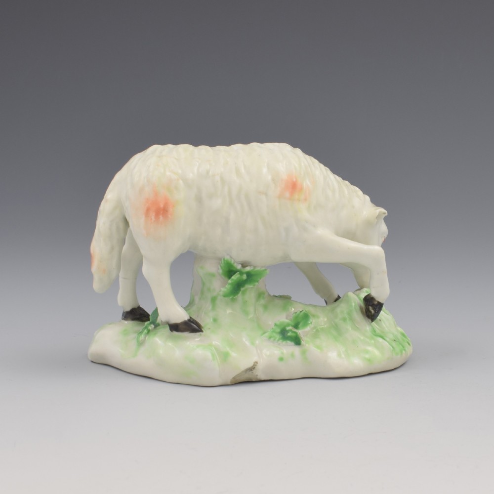 An 18th-century Derby porcelain figure depicting a white grazing ewe with orange flecks on a green leaf-patterned base. View VI