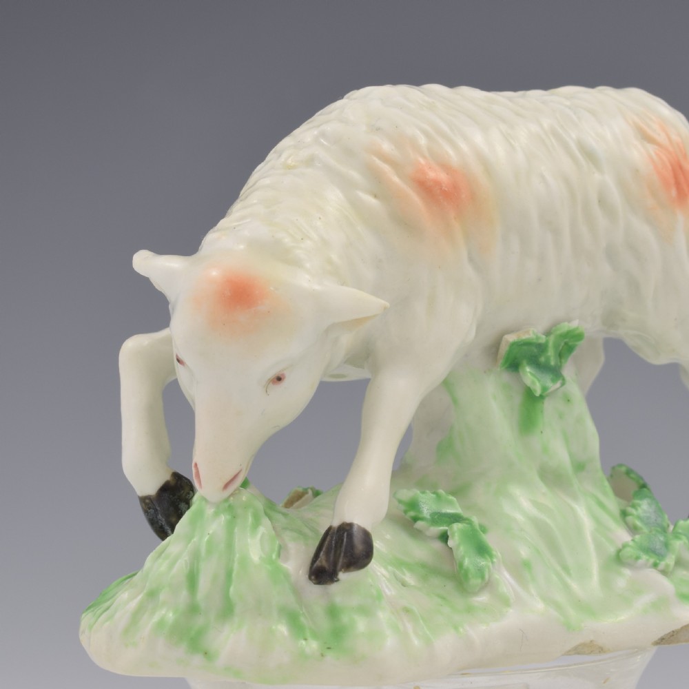 An 18th-century Derby porcelain figure depicting a white grazing ewe with orange flecks on a green leaf-patterned base. View XI