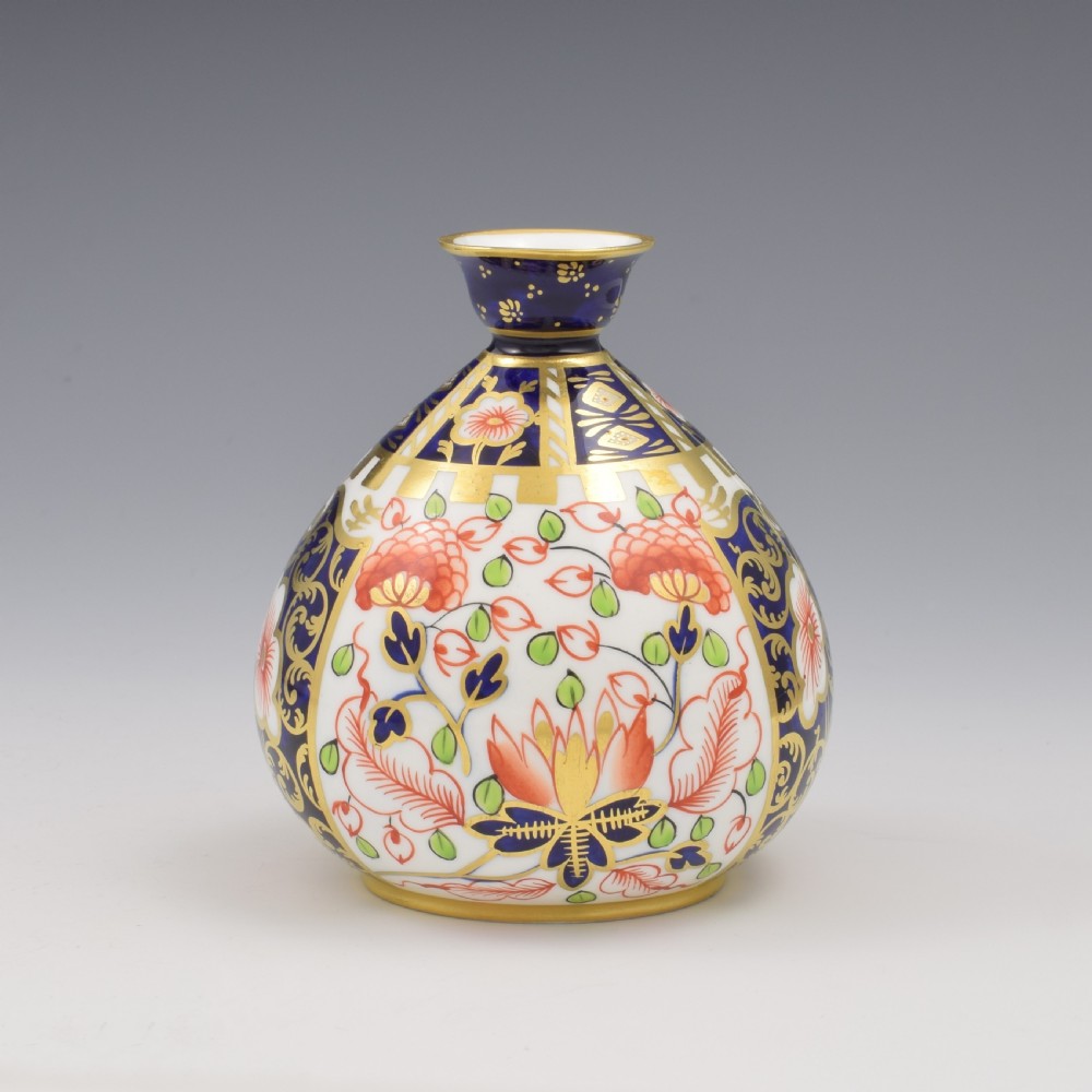 A globular Edwardian Royal Crown Derby porcelain bud vase decorated in an Imari pattern of cobalt blue, iron red flowers, green leaves, and gold gilding.