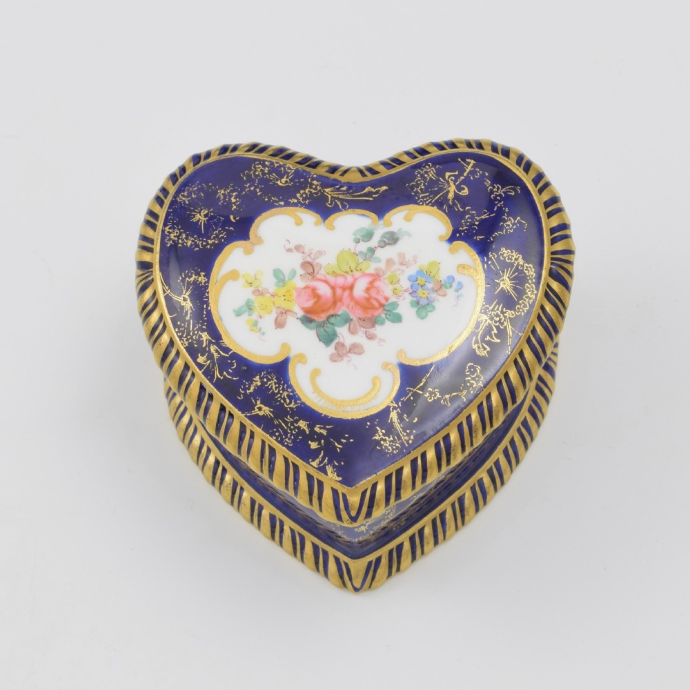 A heart-shaped cobalt blue porcelain jewellery box featuring a hand-painted floral cartouche and detailed gilding along ribbed edges.