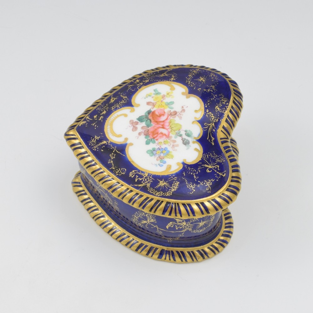 A heart-shaped cobalt blue porcelain jewellery box featuring a hand-painted floral cartouche and detailed gilding along ribbed edges. View VI