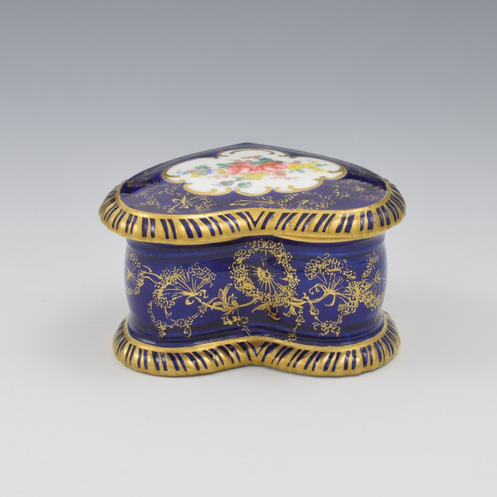 A heart-shaped cobalt blue porcelain jewellery box featuring a hand-painted floral cartouche and detailed gilding along ribbed edges. View VII