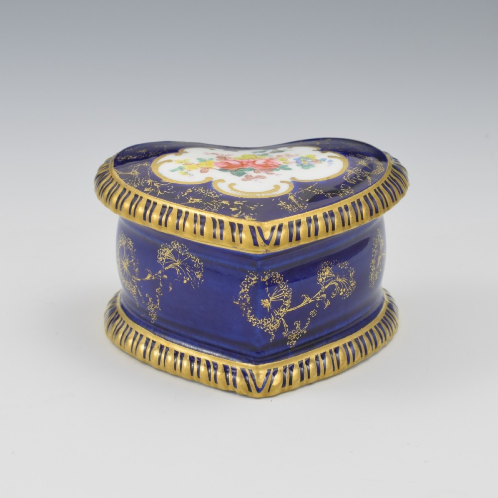 A heart-shaped cobalt blue porcelain jewellery box featuring a hand-painted floral cartouche and detailed gilding along ribbed edges. View IX