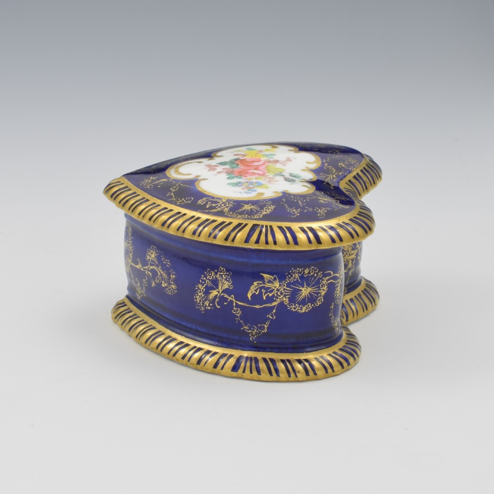 A heart-shaped cobalt blue porcelain jewellery box featuring a hand-painted floral cartouche and detailed gilding along ribbed edges. View X