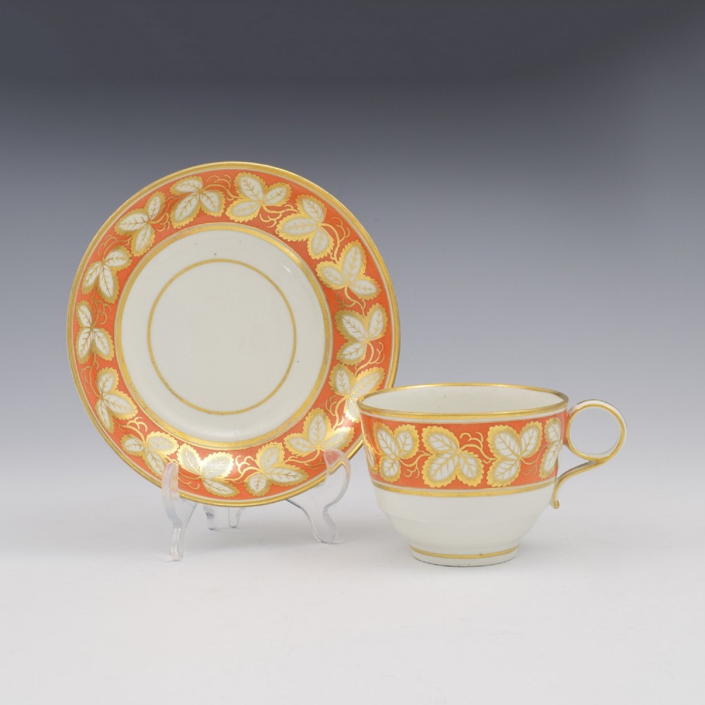 An early 19th-century Worcester porcelain tea cup and saucer featuring an orange border decorated with gilded leaf motifs on a white ground.