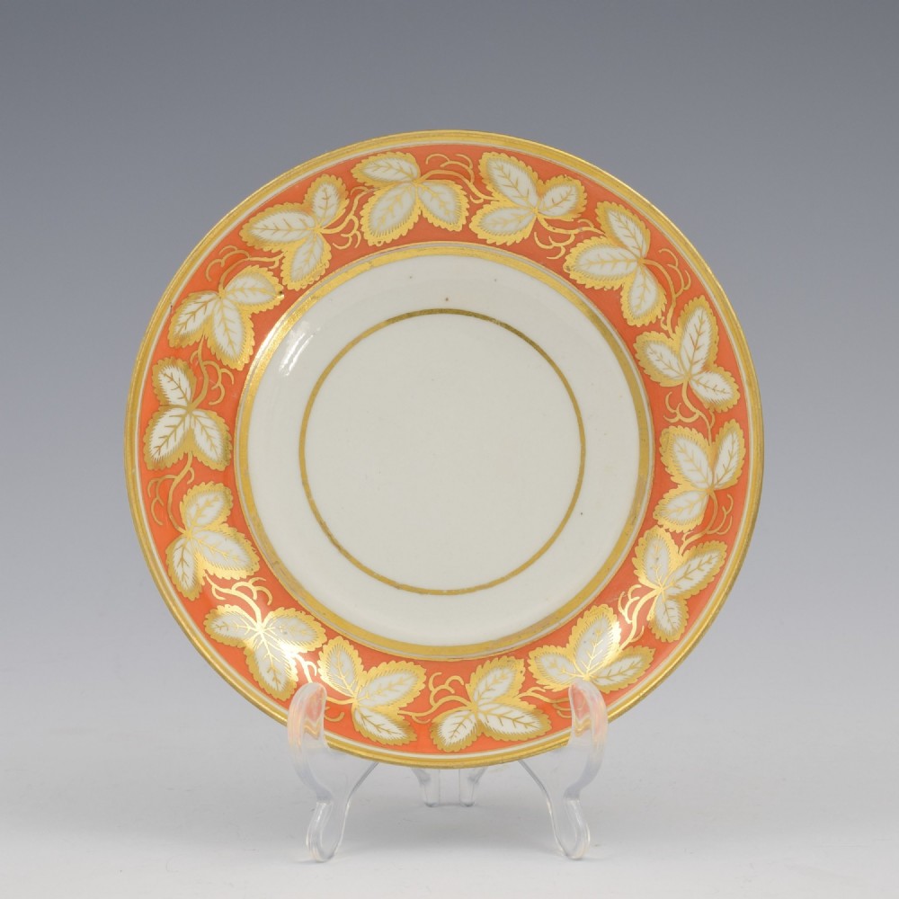 An early 19th-century Worcester porcelain tea cup and saucer featuring an orange border decorated with gilded leaf motifs on a white ground. View II