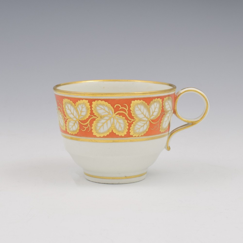 An early 19th-century Worcester porcelain tea cup and saucer featuring an orange border decorated with gilded leaf motifs on a white ground. View III