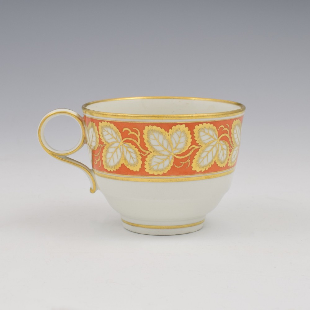 An early 19th-century Worcester porcelain tea cup and saucer featuring an orange border decorated with gilded leaf motifs on a white ground. View V