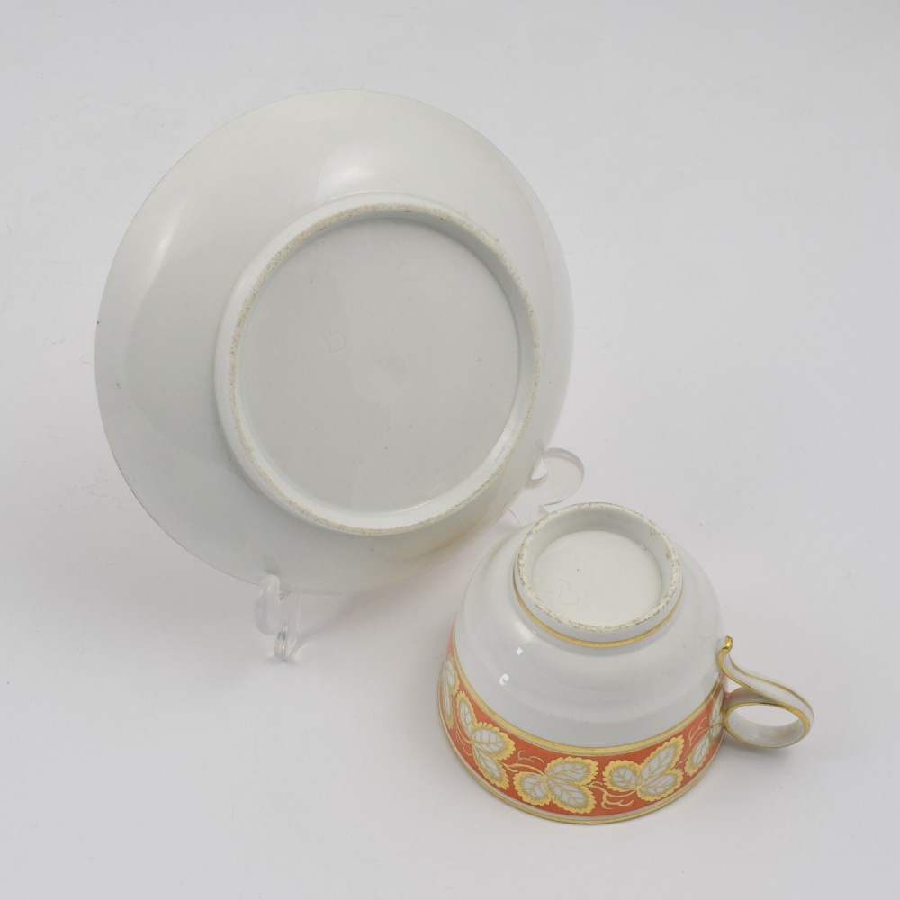 An early 19th-century Worcester porcelain tea cup and saucer featuring an orange border decorated with gilded leaf motifs on a white ground. View VII