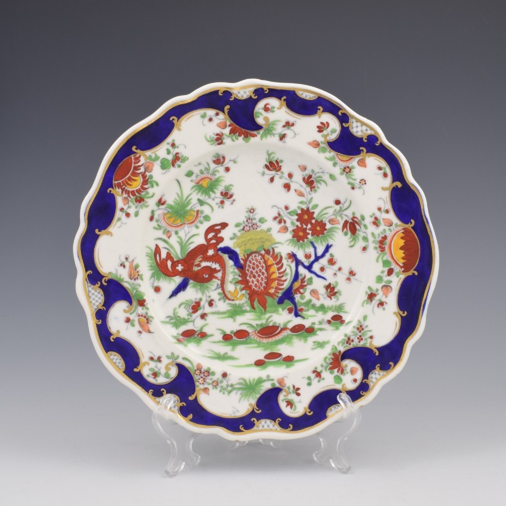 A lobed porcelain dessert plate featuring a rich cobalt blue border with gilded scrollwork and a hand-painted central design of a mythical creature among flowers.