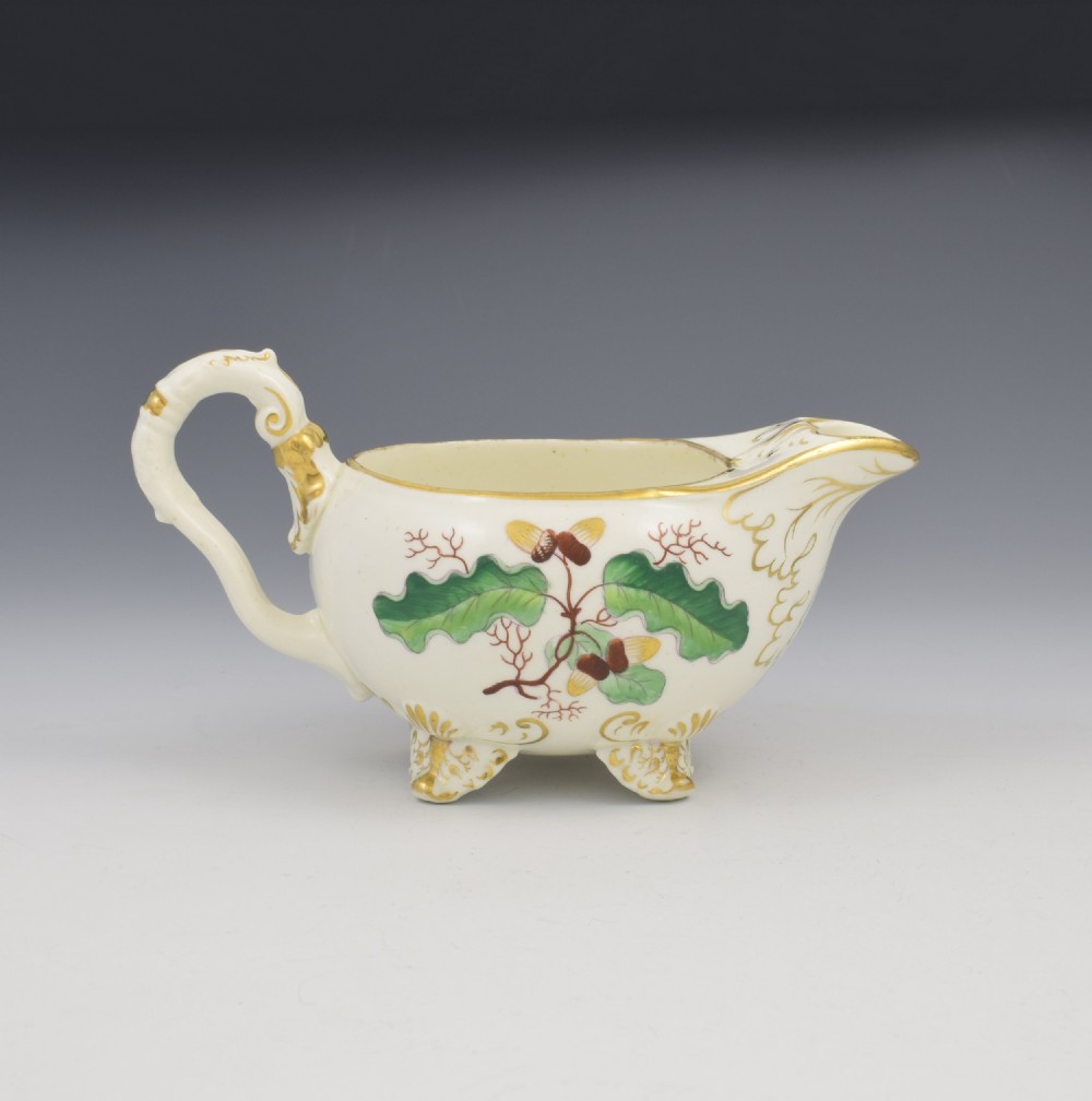 A cream-coloured Regency porcelain jug featuring hand-painted green oak leaves, brown acorns, moulded feet, and gilded trim. View II