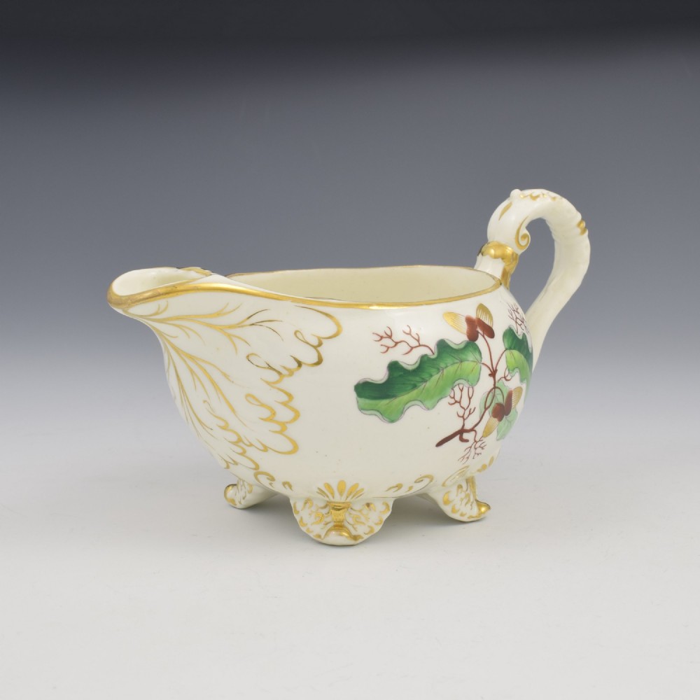 A cream-coloured Regency porcelain jug featuring hand-painted green oak leaves, brown acorns, moulded feet, and gilded trim. View V