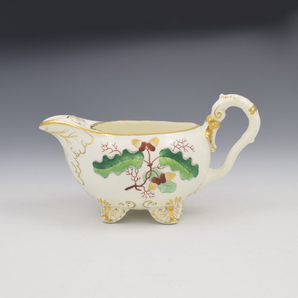 A cream-coloured Regency porcelain jug featuring hand-painted green oak leaves, brown acorns, moulded feet, and gilded trim. View VI