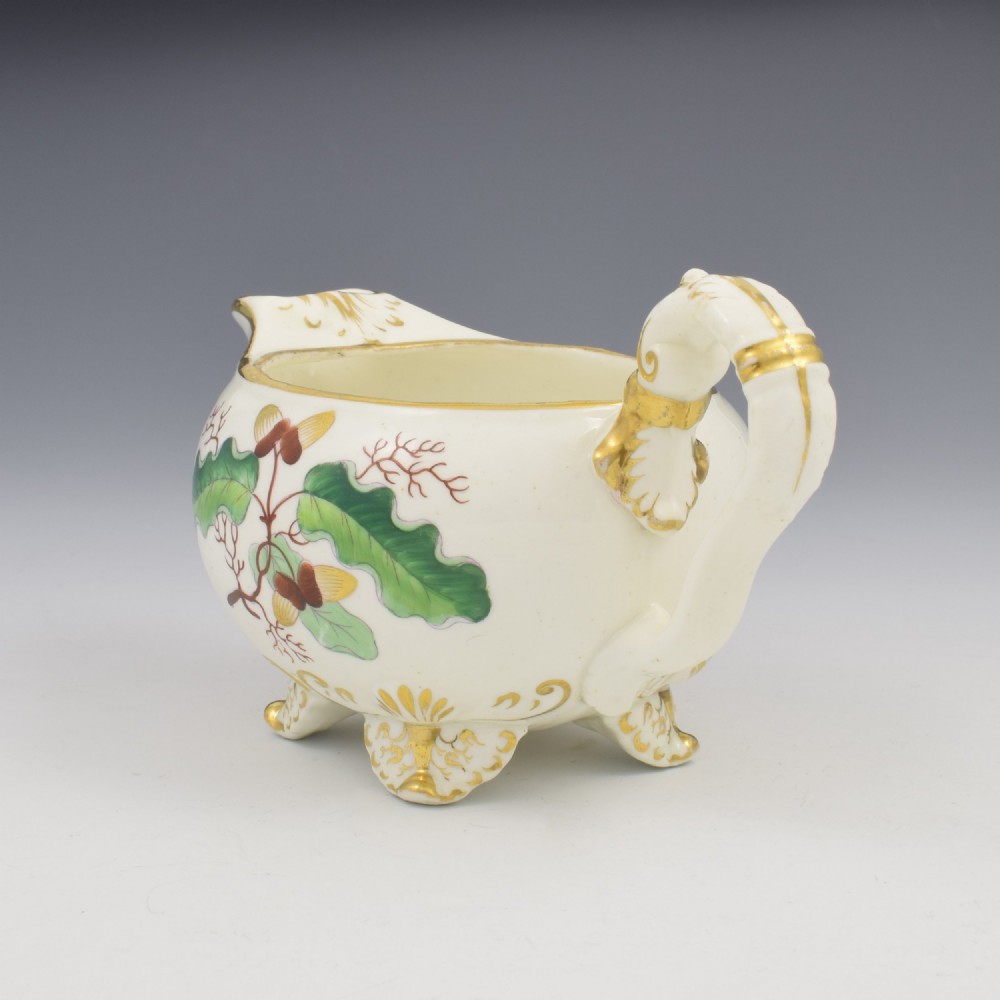 A cream-coloured Regency porcelain jug featuring hand-painted green oak leaves, brown acorns, moulded feet, and gilded trim. View VII