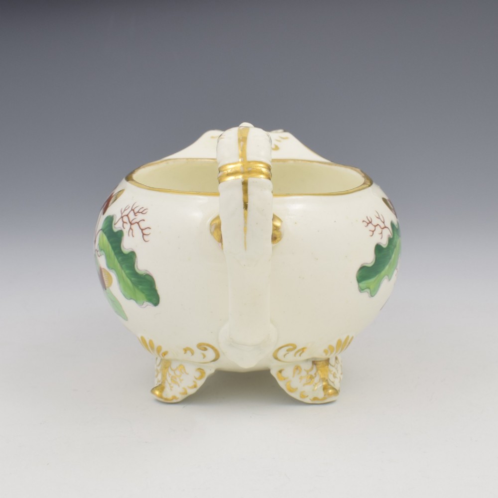 A cream-coloured Regency porcelain jug featuring hand-painted green oak leaves, brown acorns, moulded feet, and gilded trim. View VIII
