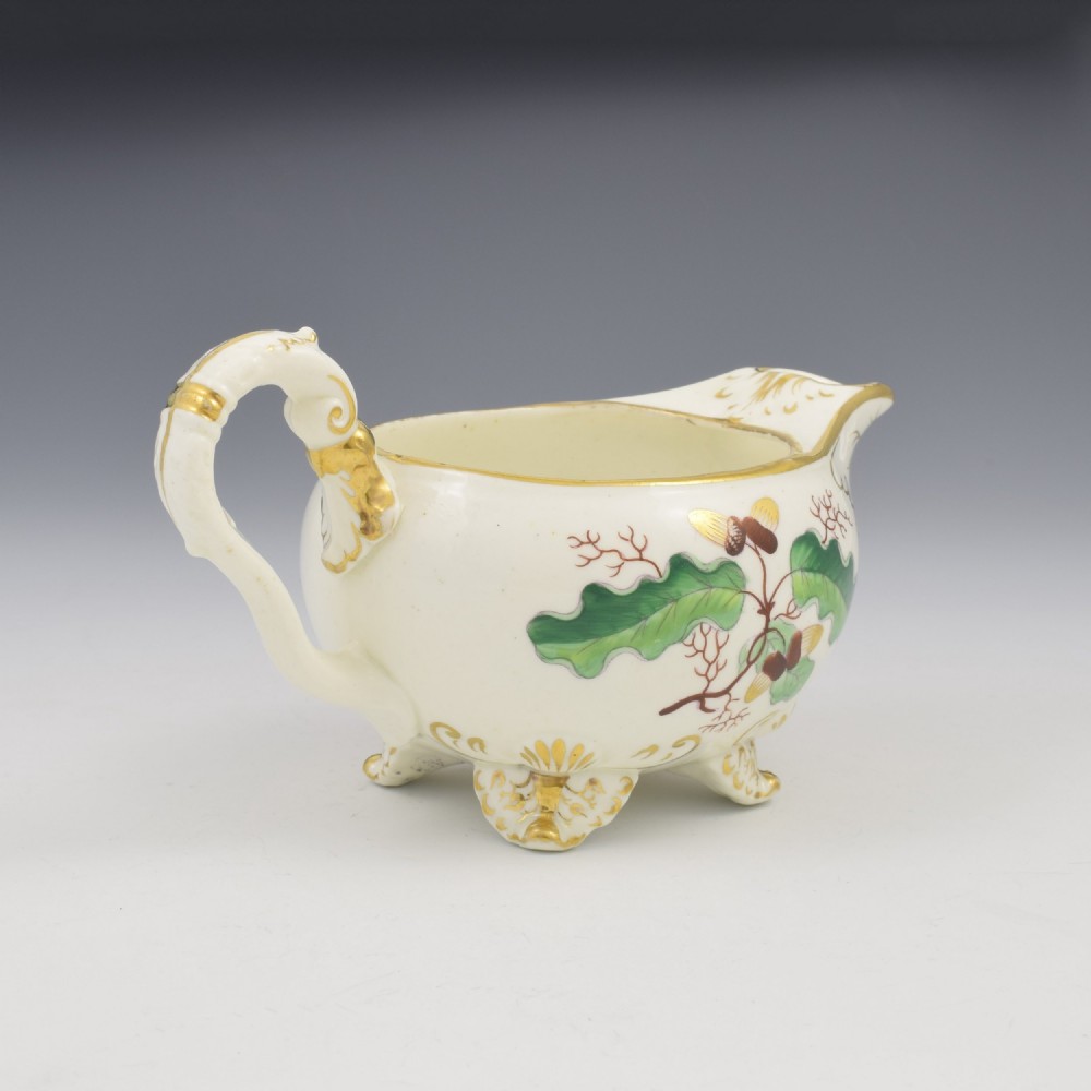A cream-coloured Regency porcelain jug featuring hand-painted green oak leaves, brown acorns, moulded feet, and gilded trim. View IX