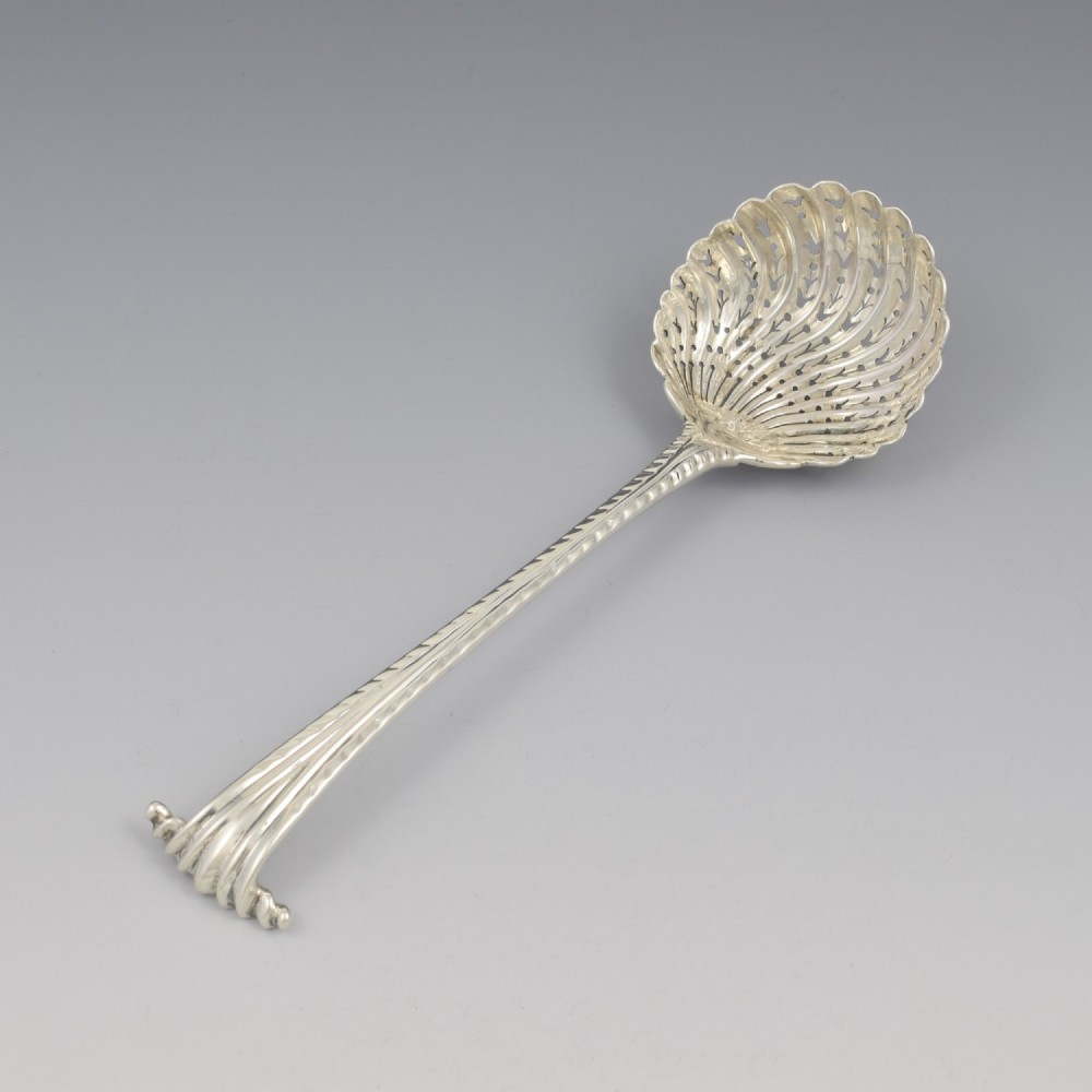 An 18th-century sterling silver sifter spoon featuring an Onslow scroll terminal, feather-edge shaft, and a pierced shell bowl.