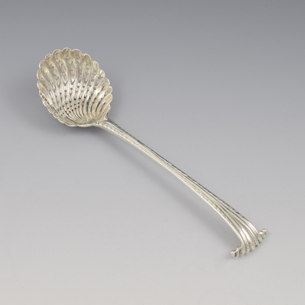 An 18th-century sterling silver sifter spoon featuring an Onslow scroll terminal, feather-edge shaft, and a pierced shell bowl. View II