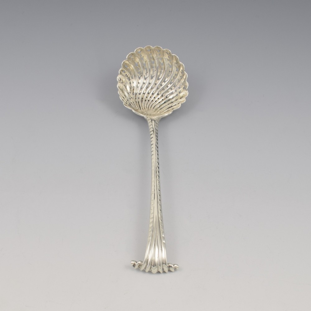 An 18th-century sterling silver sifter spoon featuring an Onslow scroll terminal, feather-edge shaft, and a pierced shell bowl. View IV