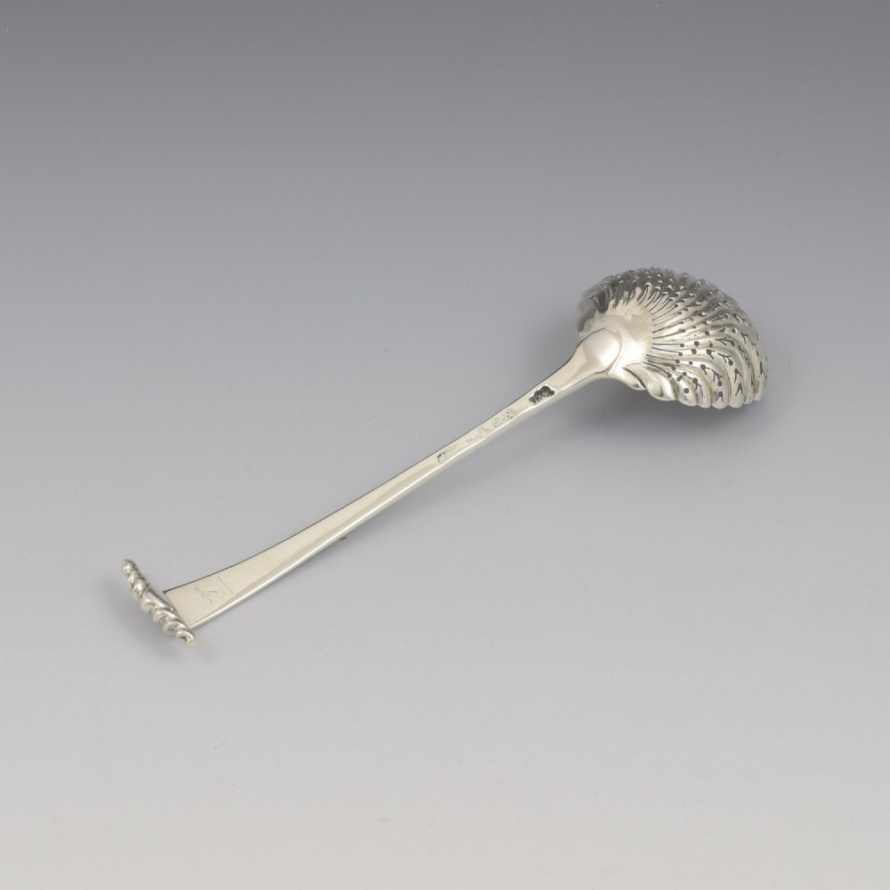 An 18th-century sterling silver sifter spoon featuring an Onslow scroll terminal, feather-edge shaft, and a pierced shell bowl. View VI