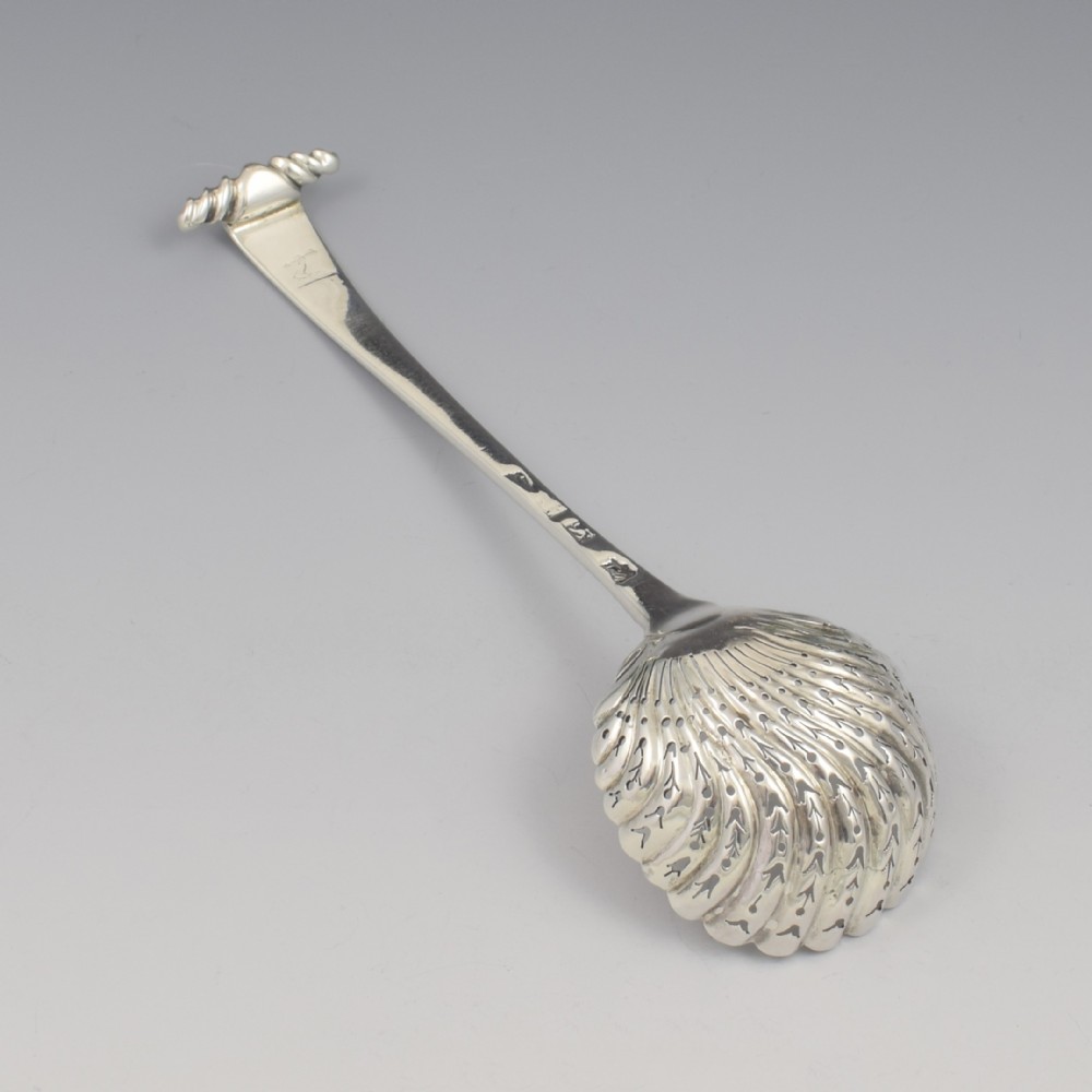 An 18th-century sterling silver sifter spoon featuring an Onslow scroll terminal, feather-edge shaft, and a pierced shell bowl. View VII