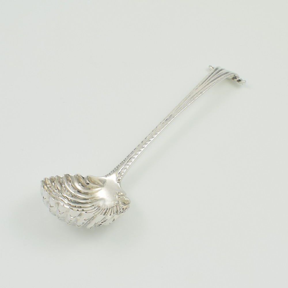 An 18th-century sterling silver sifter spoon featuring an Onslow scroll terminal, feather-edge shaft, and a pierced shell bowl. View X