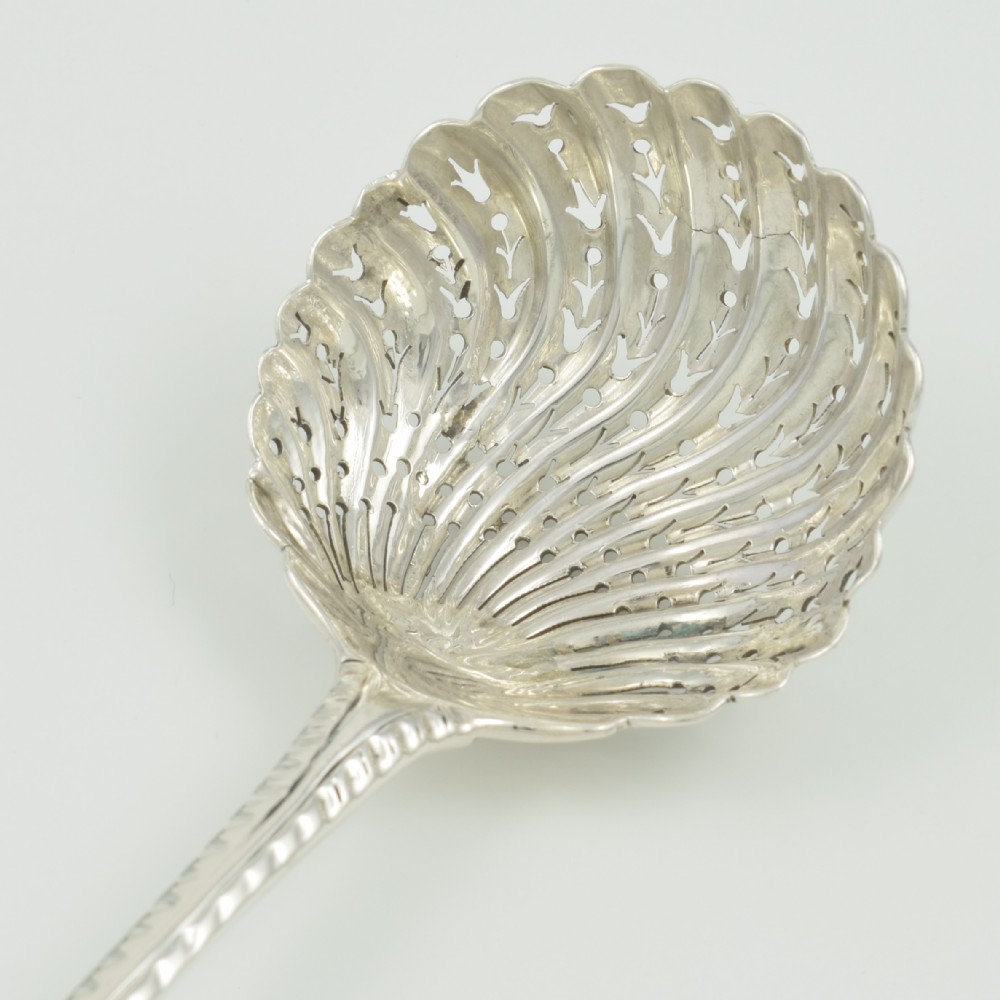 An 18th-century sterling silver sifter spoon featuring an Onslow scroll terminal, feather-edge shaft, and a pierced shell bowl. View XIII