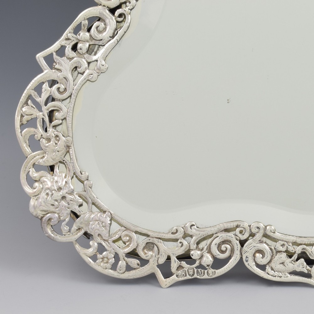 An antique silver dressing table mirror featuring intricate pierced scrollwork, foliage, bird motifs, and a mascaron crest around a shaped glass plate. View IV