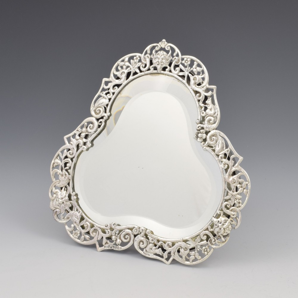 An antique silver dressing table mirror featuring intricate pierced scrollwork, foliage, bird motifs, and a mascaron crest around a shaped glass plate. View VII