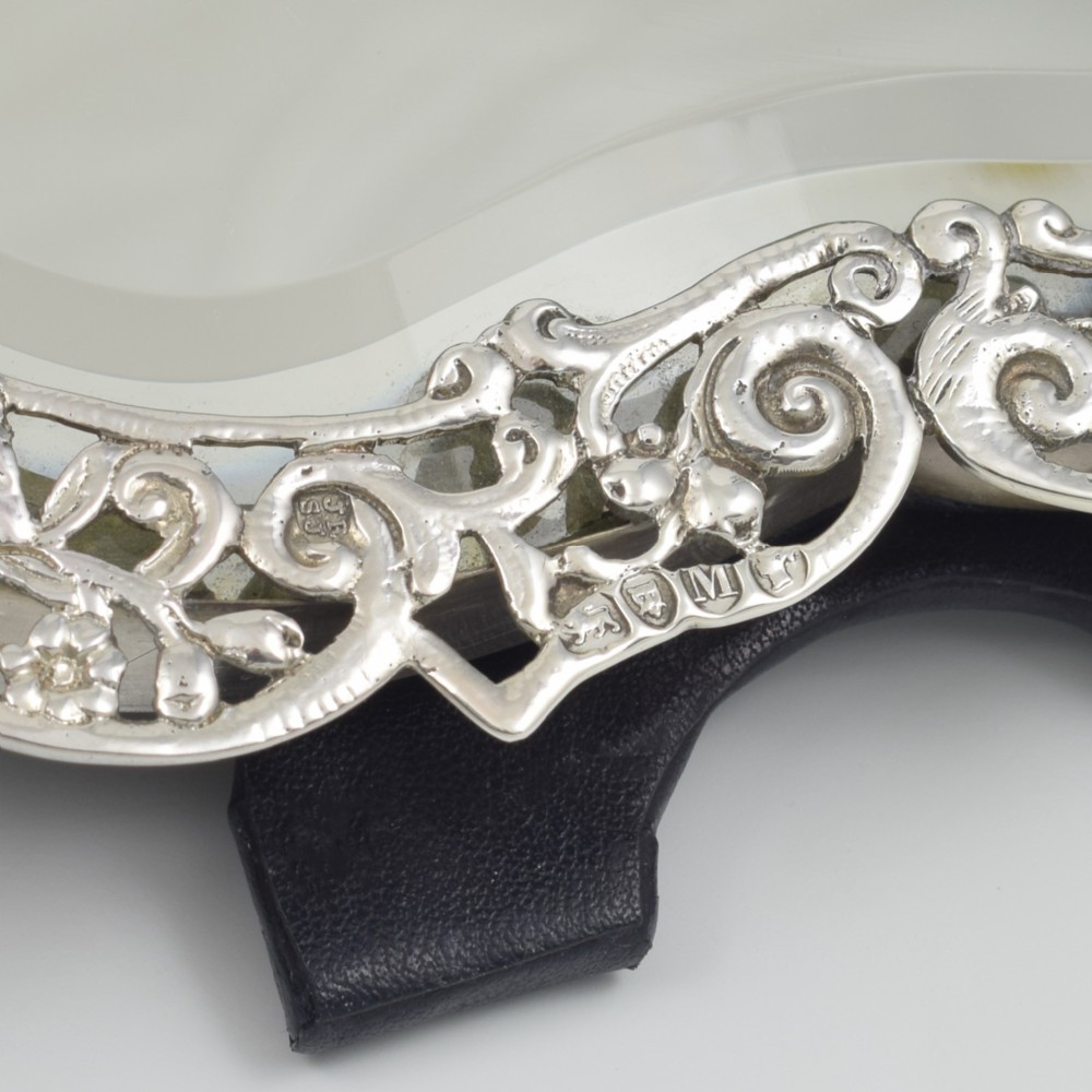 An antique silver dressing table mirror featuring intricate pierced scrollwork, foliage, bird motifs, and a mascaron crest around a shaped glass plate. View XII