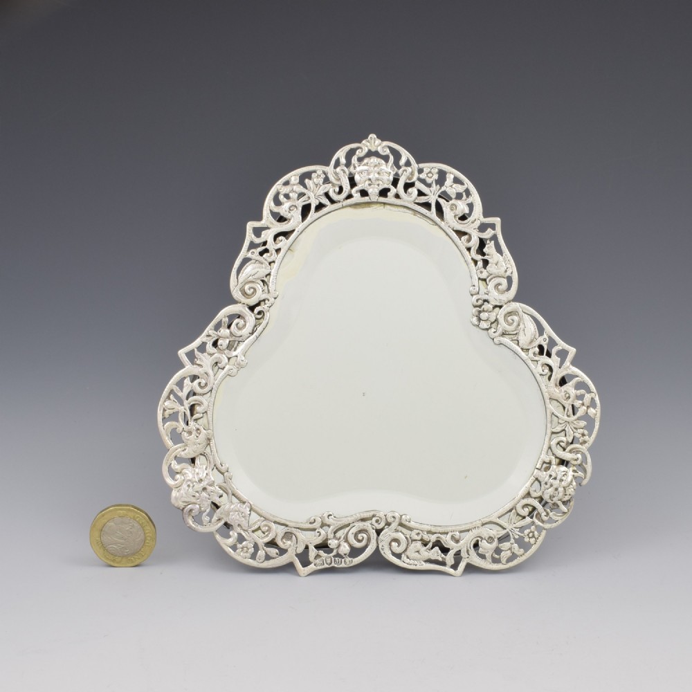An antique silver dressing table mirror featuring intricate pierced scrollwork, foliage, bird motifs, and a mascaron crest around a shaped glass plate. View XIII
