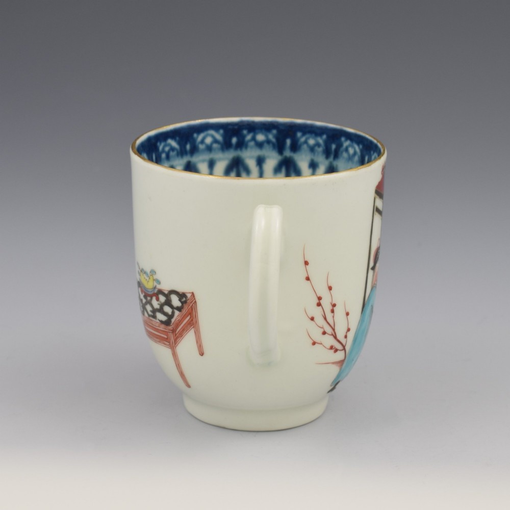 An 18th-century white porcelain coffee cup decorated with hand-painted Chinese figures in red and blue enamel, featuring a single handle and an internal patterned rim. View V