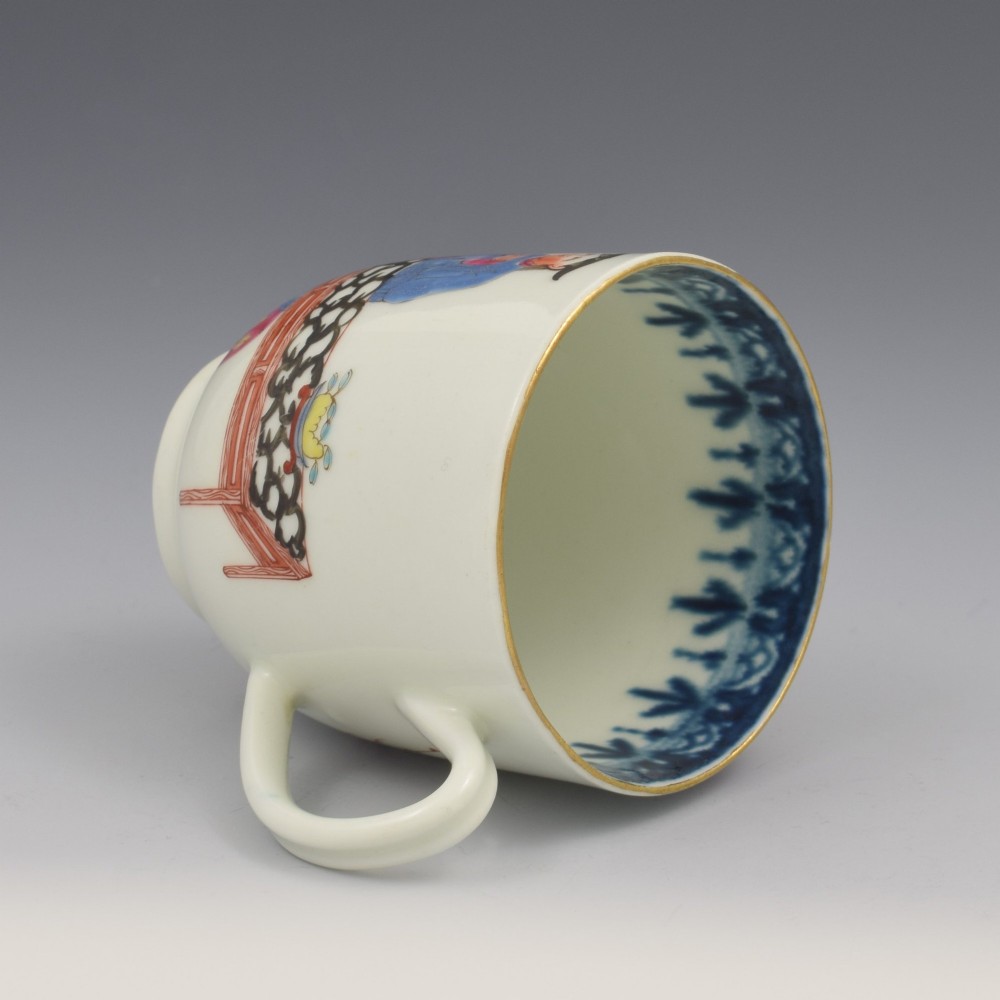 An 18th-century white porcelain coffee cup decorated with hand-painted Chinese figures in red and blue enamel, featuring a single handle and an internal patterned rim. View VI