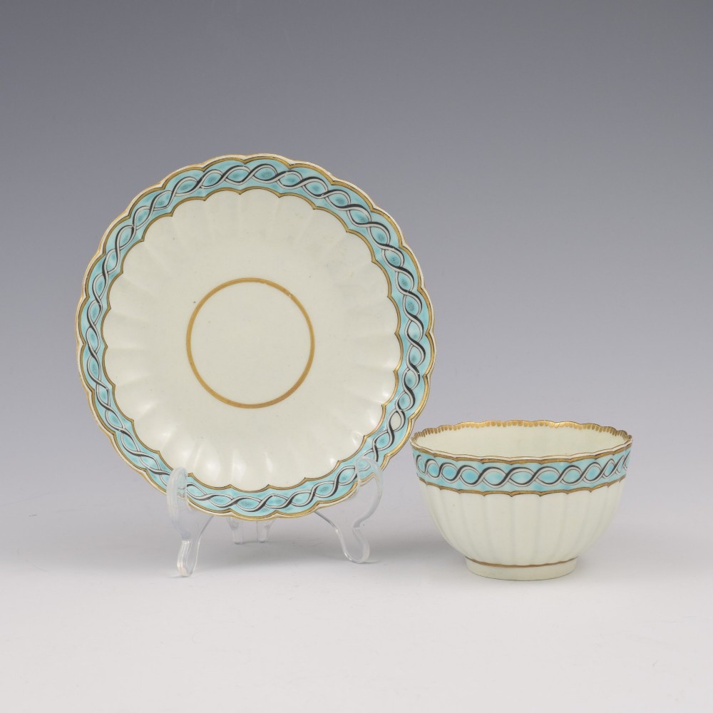 An eighteenth-century Worcester soft-paste porcelain fluted tea bowl and saucer featuring a turquoise and black guilloche border with gilded rim details.