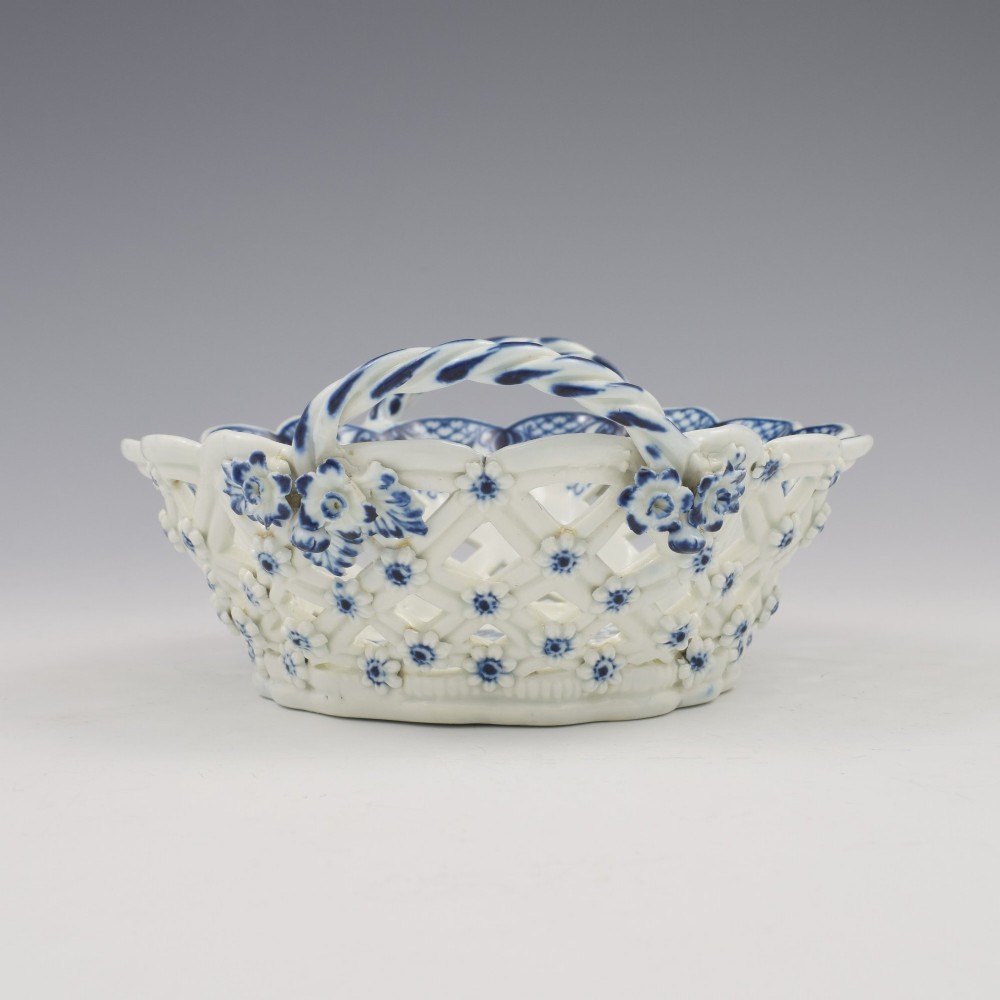 An 18th-century oval blue and white soft-paste porcelain basket with reticulated lattice sides, twisted rope handles, and an underglaze floral pine cone pattern. View IX