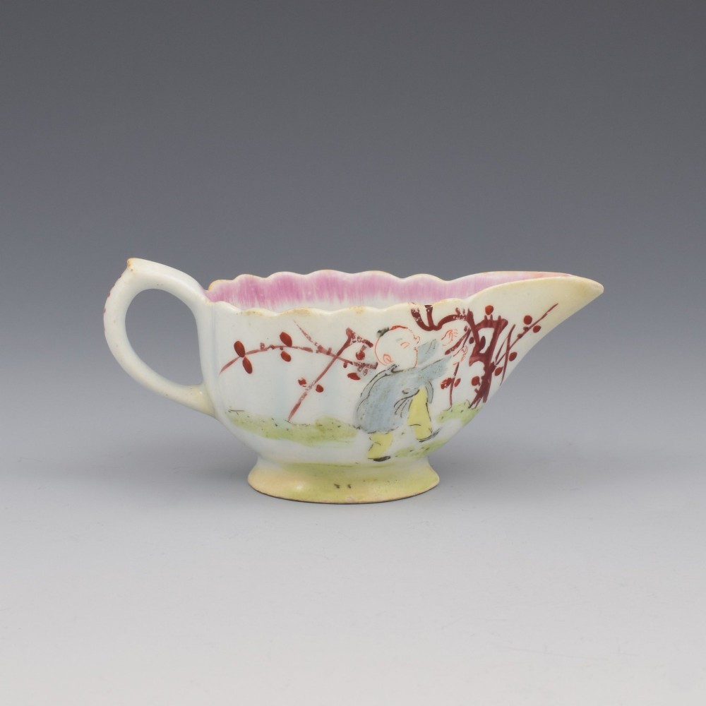A small 18th-century soft-paste porcelain sauce boat featuring a scalloped fluted rim, loop handle, and hand-painted Chinoiserie figures with a pink interior border.