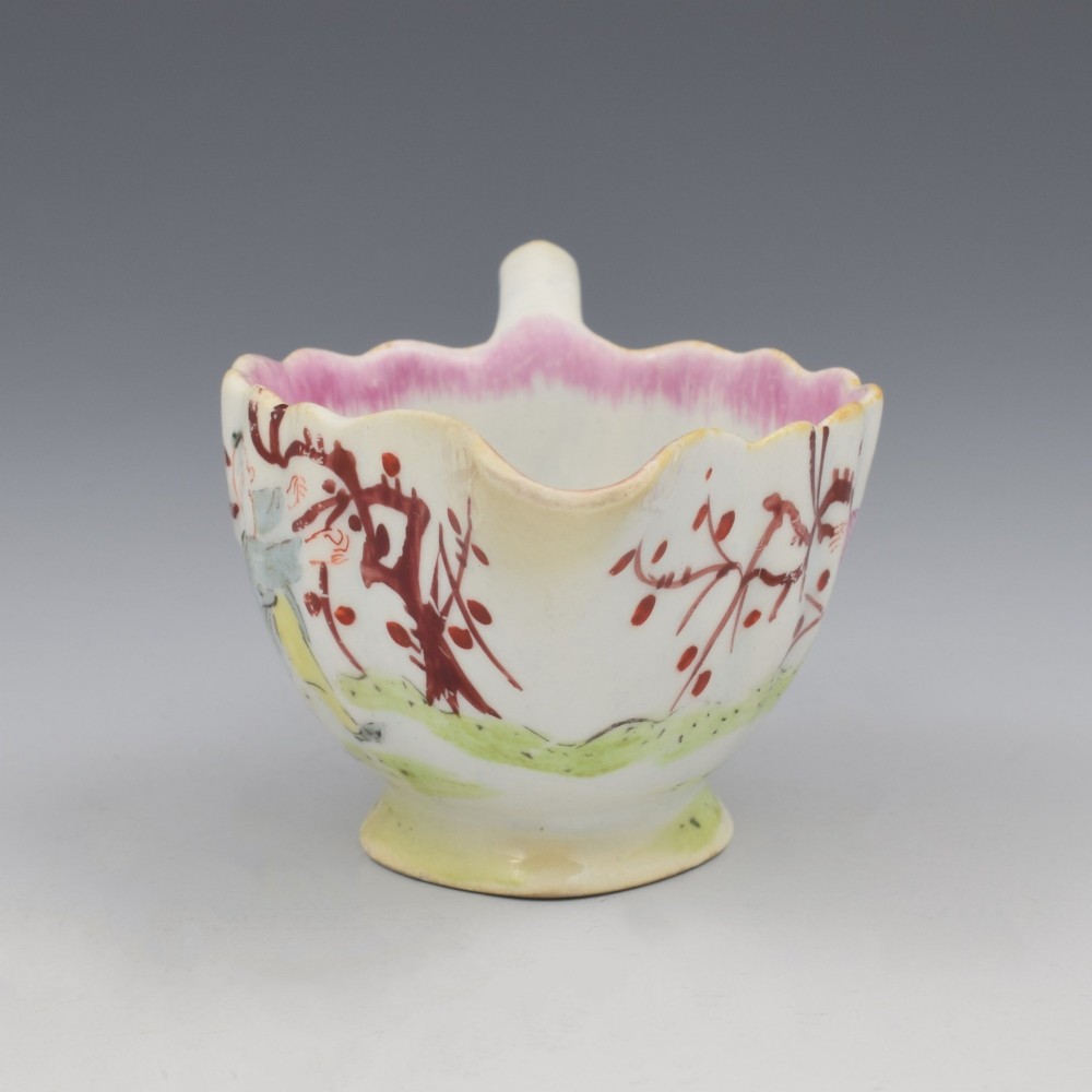 A small 18th-century soft-paste porcelain sauce boat featuring a scalloped fluted rim, loop handle, and hand-painted Chinoiserie figures with a pink interior border. View III
