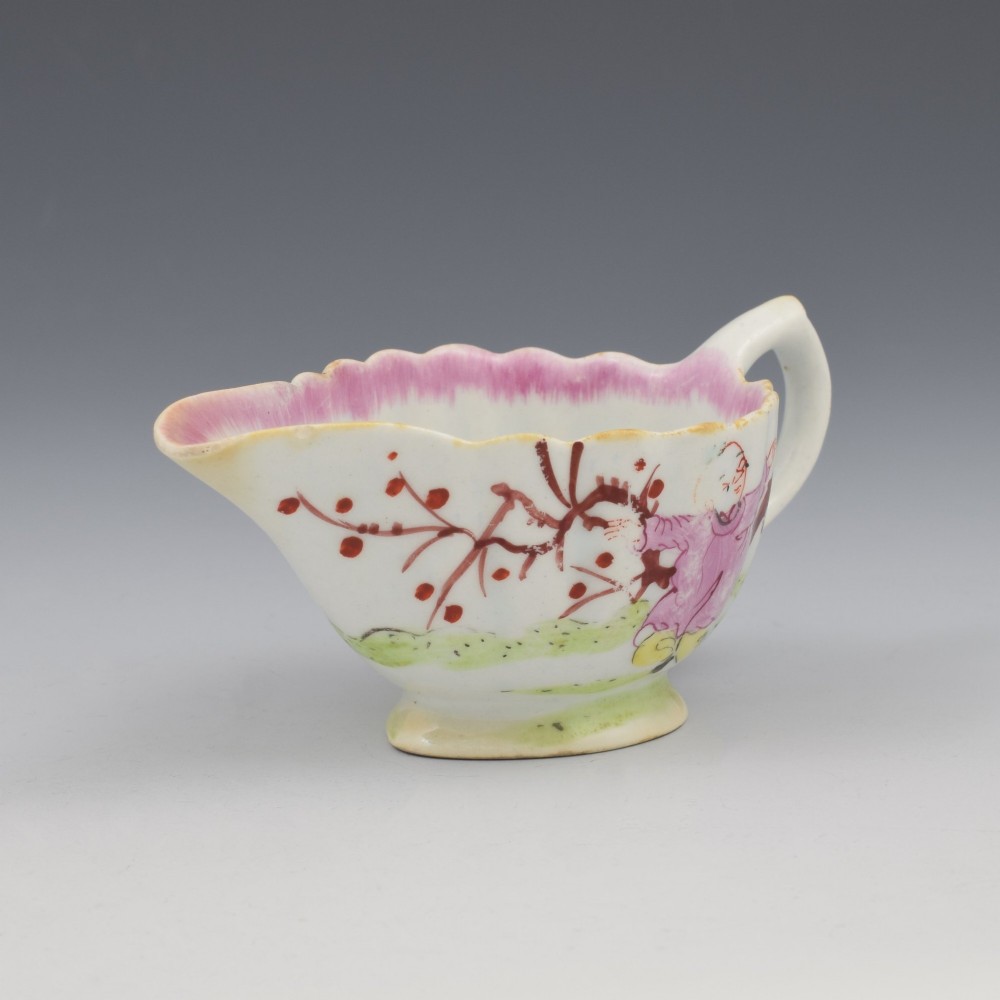 A small 18th-century soft-paste porcelain sauce boat featuring a scalloped fluted rim, loop handle, and hand-painted Chinoiserie figures with a pink interior border. View IV