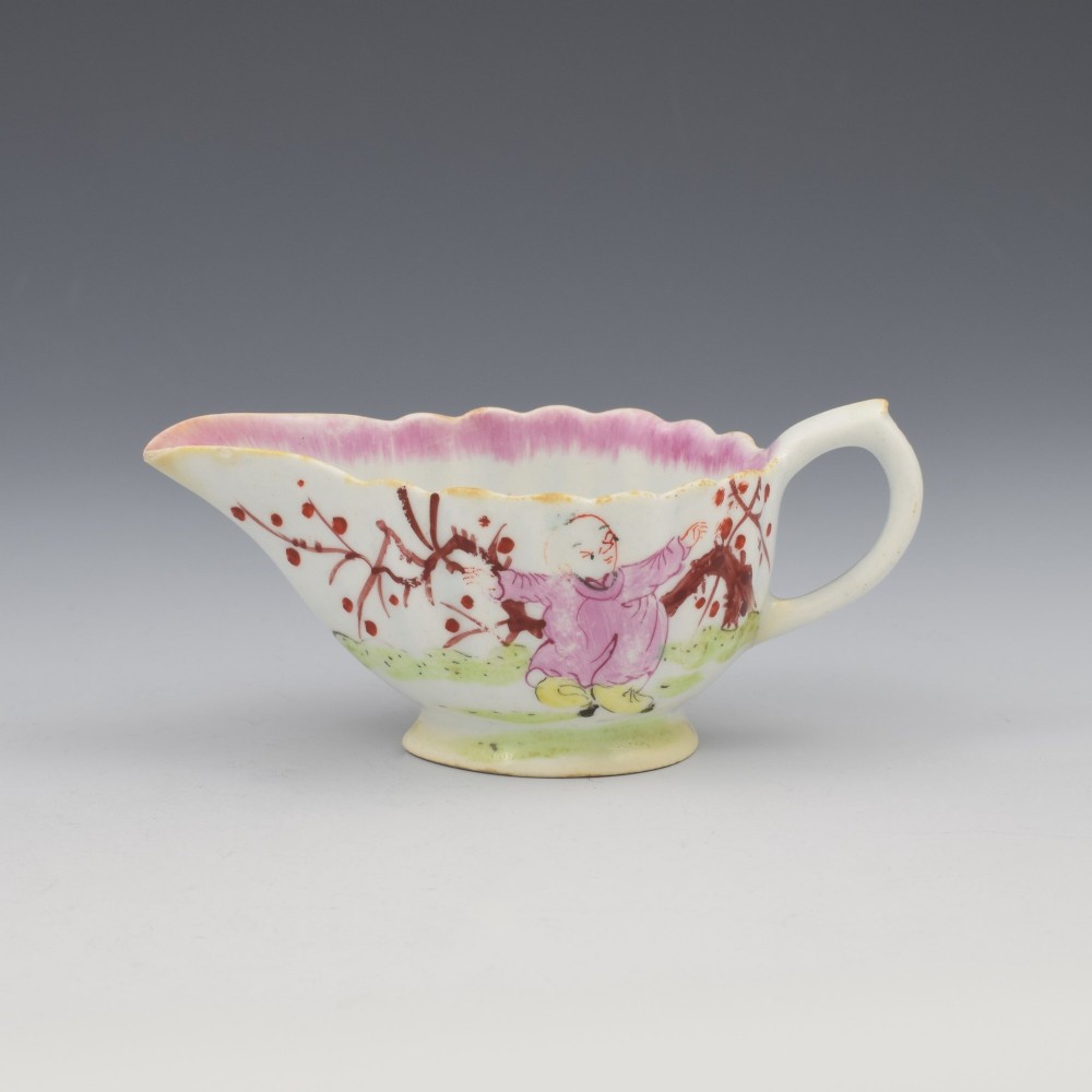 A small 18th-century soft-paste porcelain sauce boat featuring a scalloped fluted rim, loop handle, and hand-painted Chinoiserie figures with a pink interior border. View V