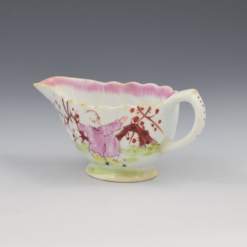 A small 18th-century soft-paste porcelain sauce boat featuring a scalloped fluted rim, loop handle, and hand-painted Chinoiserie figures with a pink interior border. View VI