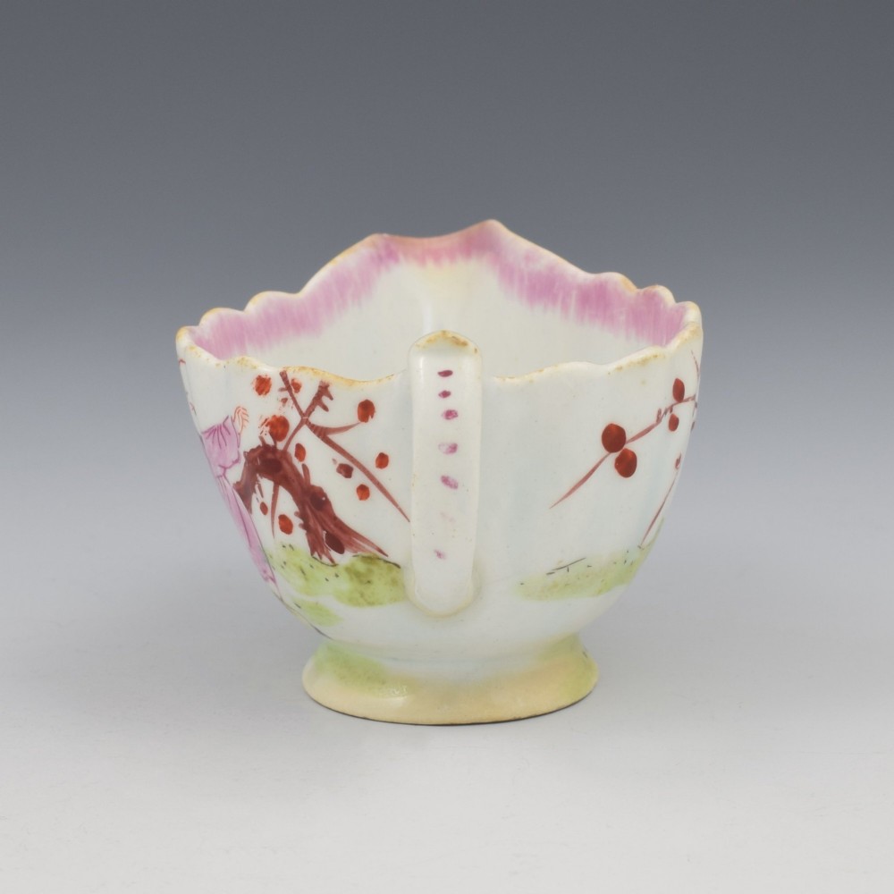 A small 18th-century soft-paste porcelain sauce boat featuring a scalloped fluted rim, loop handle, and hand-painted Chinoiserie figures with a pink interior border. View VII