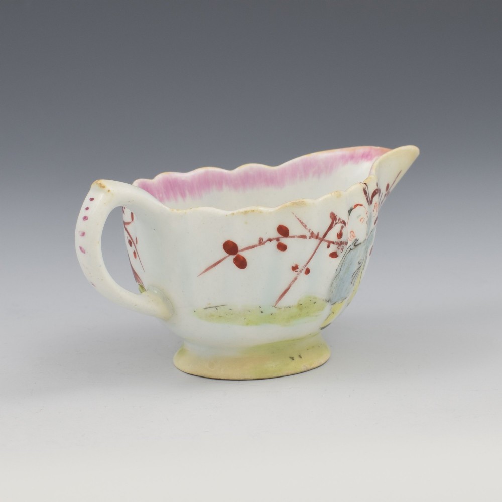 A small 18th-century soft-paste porcelain sauce boat featuring a scalloped fluted rim, loop handle, and hand-painted Chinoiserie figures with a pink interior border. View VIII